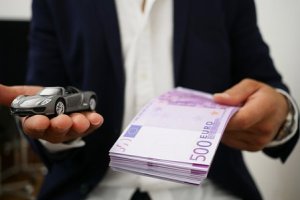 Postava muža s autíčkom a bankovkami v rukách